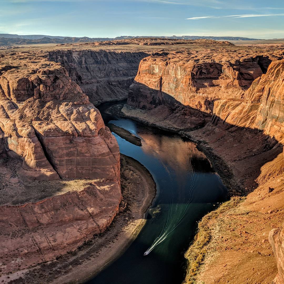 A small boat jets around the Horse Shoe bend from the right meander of the Colorado River.